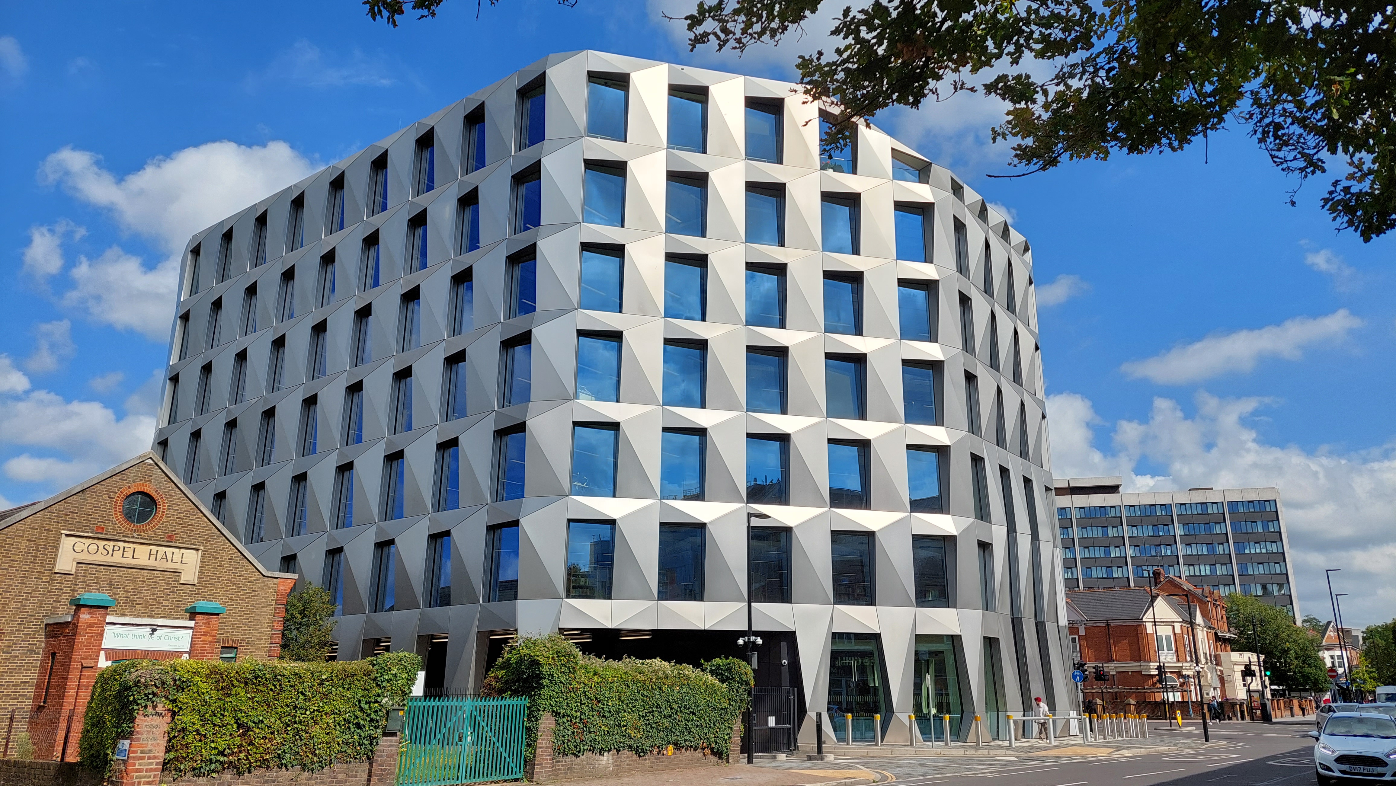 The angular white facade of Hounslow House beside the Gospel Hall, photographed from across Bath Road under a blue sky.