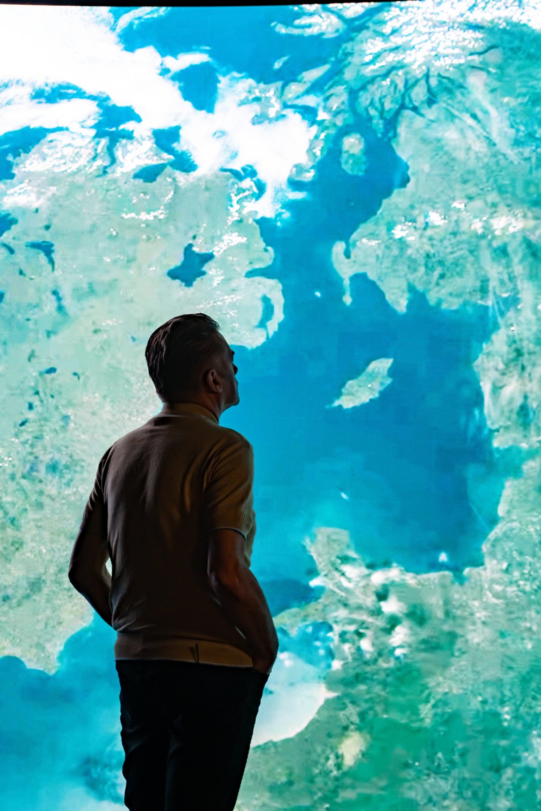 A man seen from behind facing a large screen showing Earth